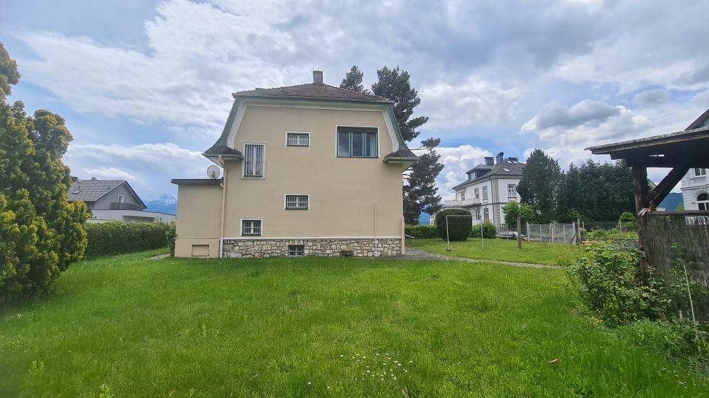 Weitläufiger Rasenbereich hinter dem Haus mit Blick auf die umliegende Landschaft und Berge.