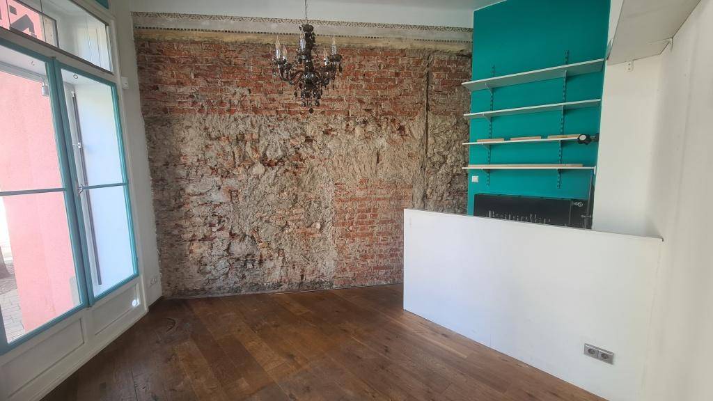 Geräumiger Innenraum mit rustikaler Ziegelwand, Holzboden und modernen Regalen an der türkisen Wand.