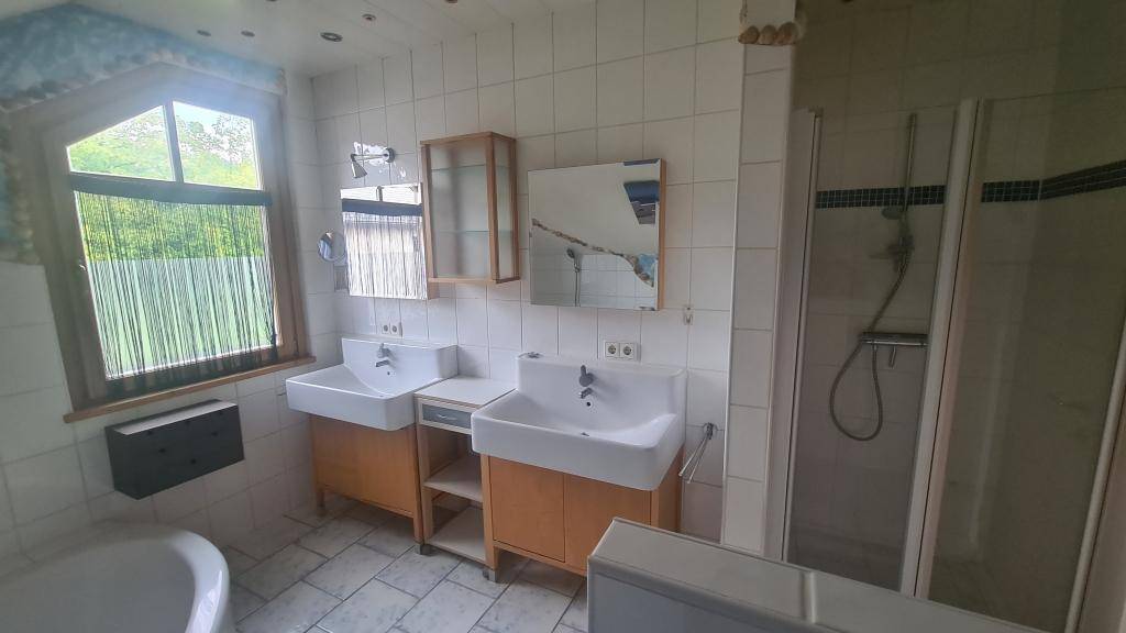 Helles Badezimmer mit Dusche, Badewanne, Doppelwaschbecken und Fenster.