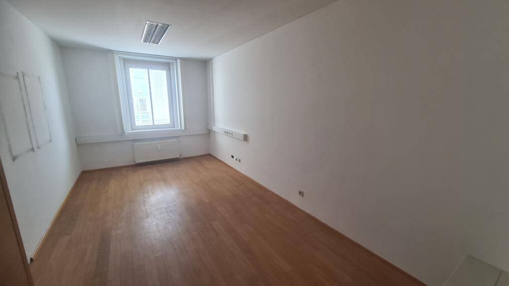 Einzelbüro mit Holzboden, großem Fenster und weiß gestrichenen Wänden, bietet eine ruhige Arbeitsumgebung.