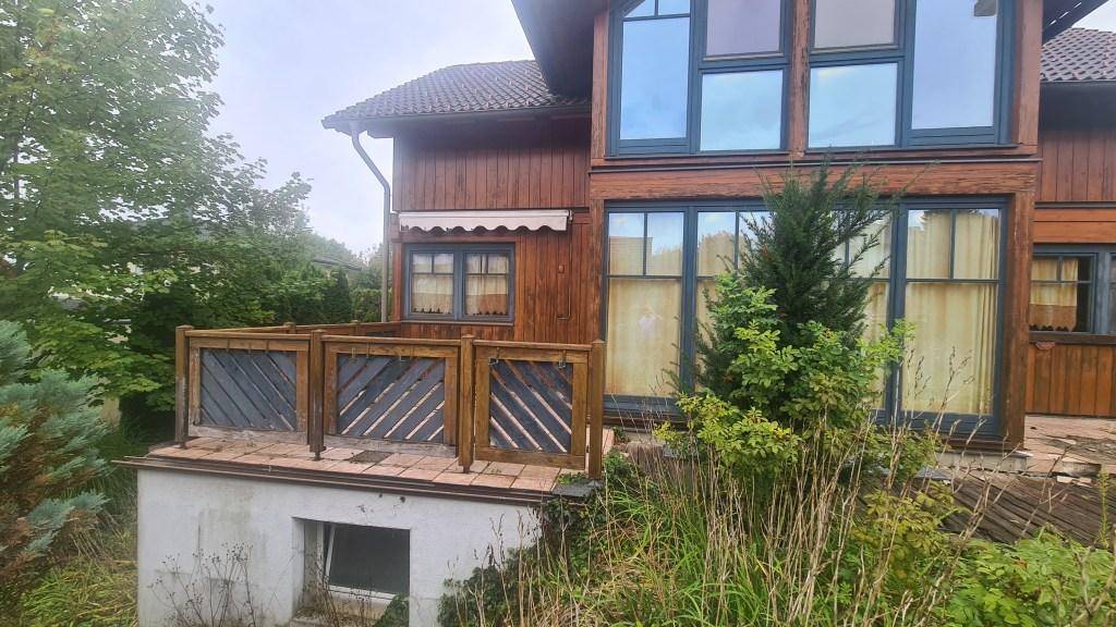 Kleine erhöhte Terrasse mit Holzgeländer und Blick auf die grüne Umgebung des Hauses.