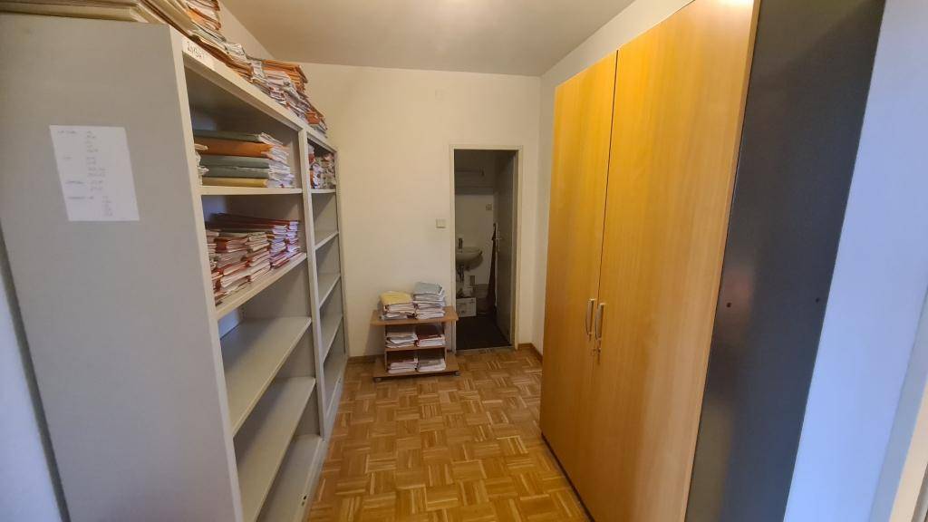 Lagerraum mit hohen Regalen, gefüllt mit Dokumenten, und einem Holzschrank.