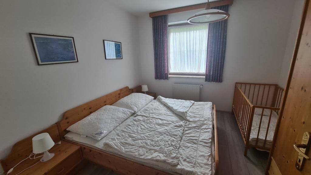 Schlafzimmer mit Doppelbett, Babybett und Holzmöbeln, bietet eine ruhige Atmosphäre.