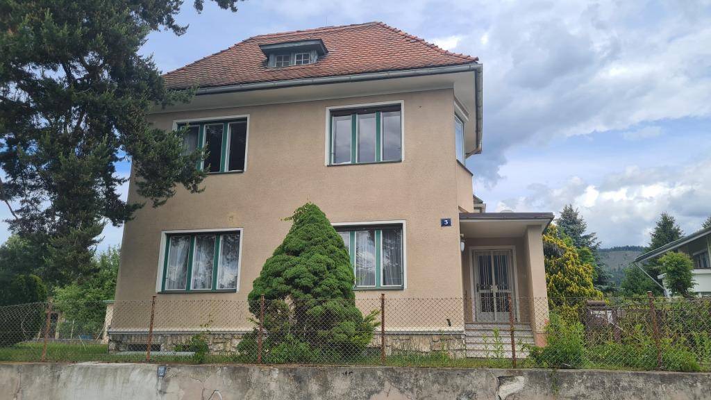 Frontansicht des Hauses mit beigefarbener Fassade, grünen Fensterrahmen und einem gepflegten Vorgarten.