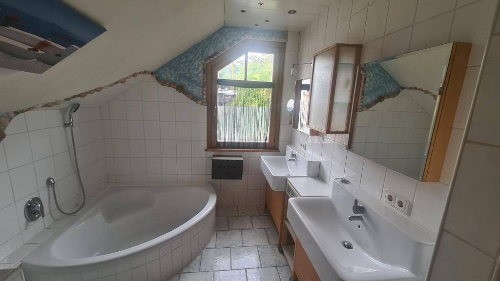 Badezimmer im Dachgeschoss mit Badewanne, Doppelwaschbecken und Fenster.