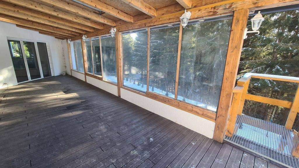 Überdachte Loggia mit Holzboden und einem schönen Blick auf den verschneiten Wald.
