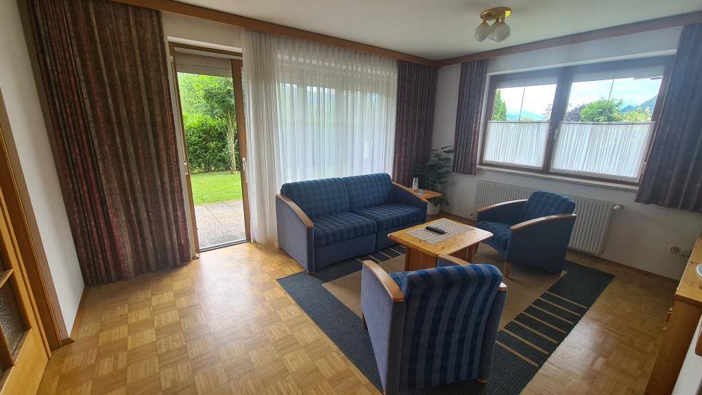 Gemütliches Wohnzimmer mit Parkettboden, blauen Sofas und Zugang zum Garten.