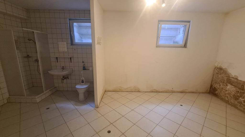 Kellerraum mit Fliesenboden, Fenster und integriertem Duschbereich mit WC.