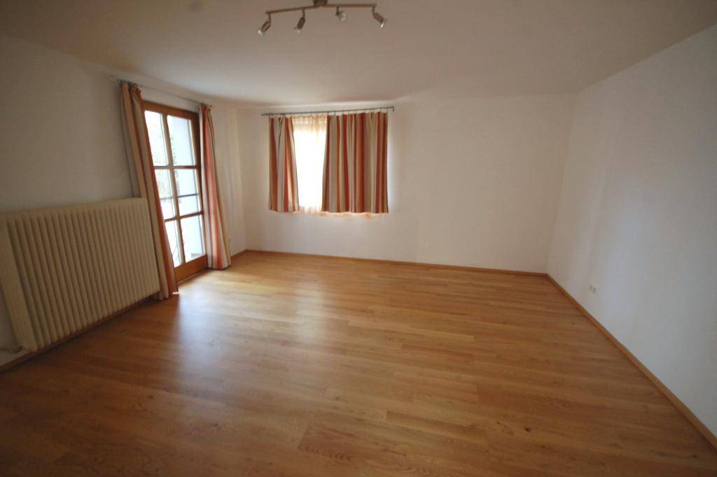 Helles Schlafzimmer mit Holzboden, Heizkörper und Zugang zu einem Balkon.