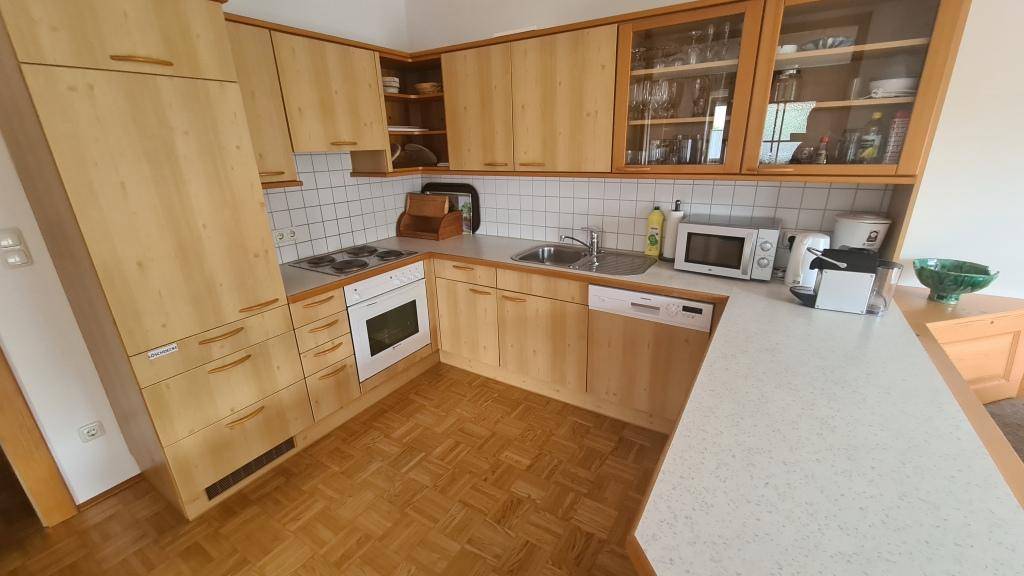 Funktionale Holzküche mit Einbaugeräten, weißen Fliesen und Parkettboden.