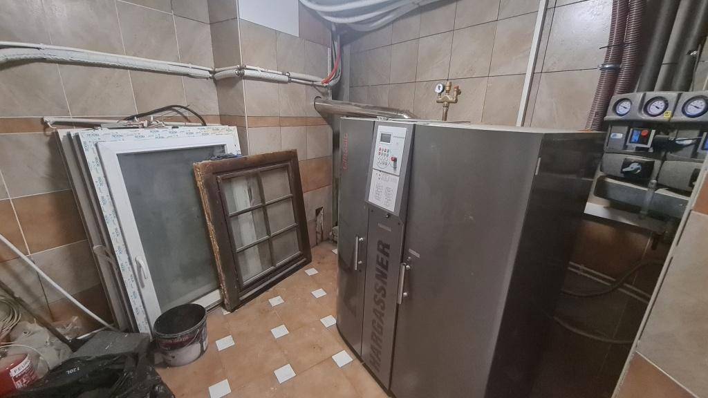 Heizungsraum mit großem Heizkessel, gefliesten Wänden und sichtbaren Rohren.