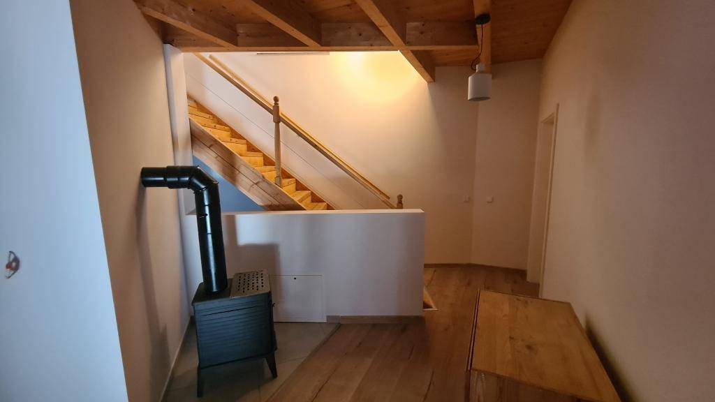 Flur mit Holztreppe, Kaminofen und sichtbaren Holzbalken an der Decke.