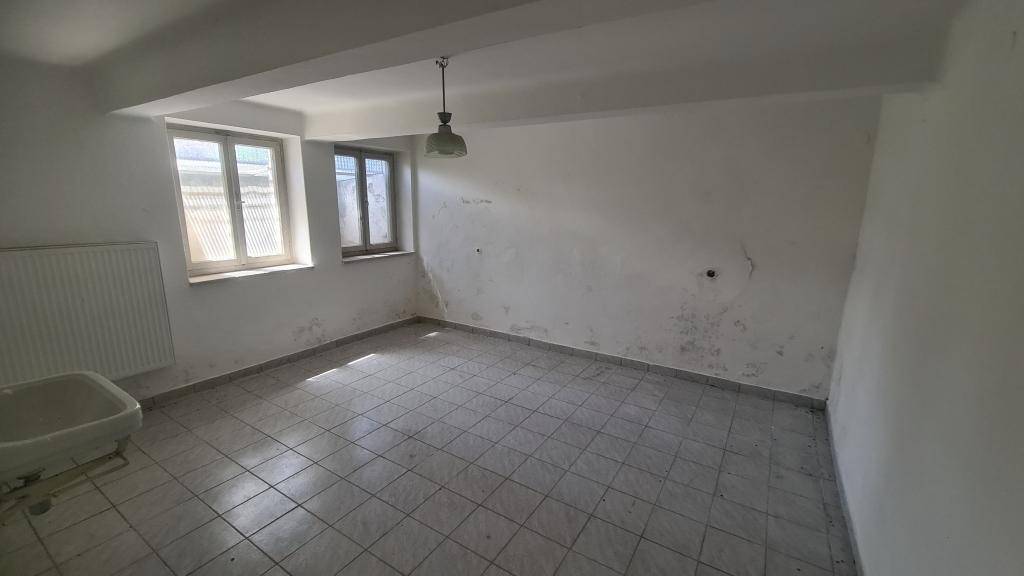Kellerraum mit Fliesenboden, Fenster und Heizkörper, renovierungsbedürftig.
