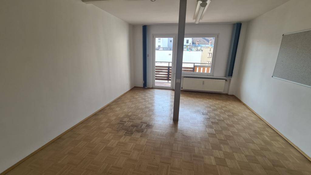 Büroraum mit Parkettboden, weiß gestrichenen Wänden und Zugang zu einem Balkon, inklusive Stützsäule.