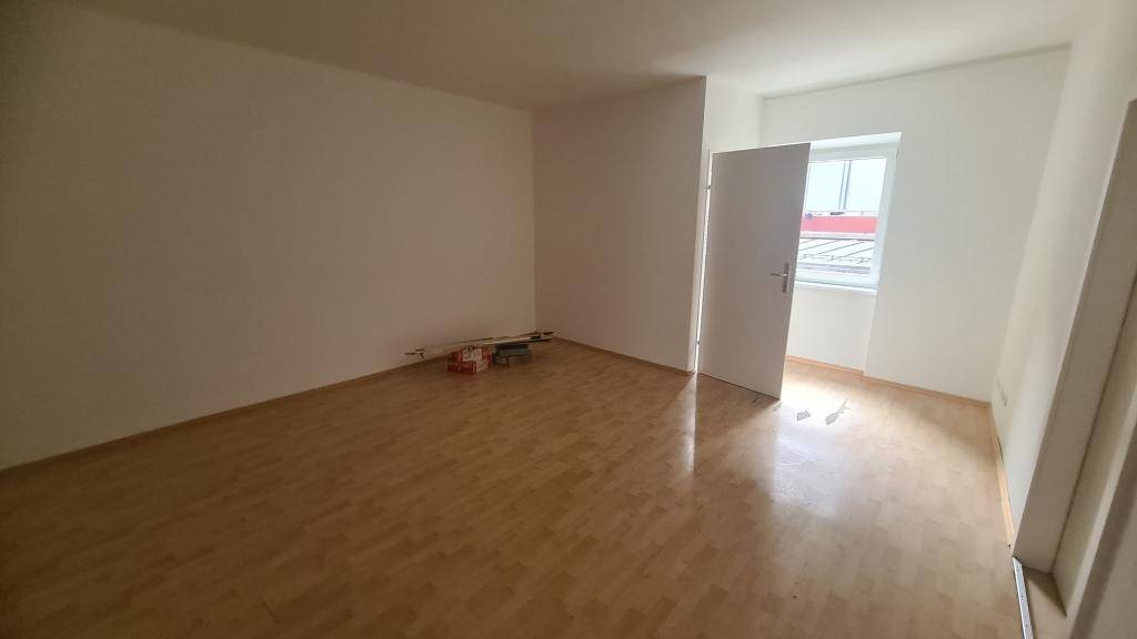 Heller Raum mit Laminatboden und einem Fenster, das ausreichend Tageslicht hereinlässt.