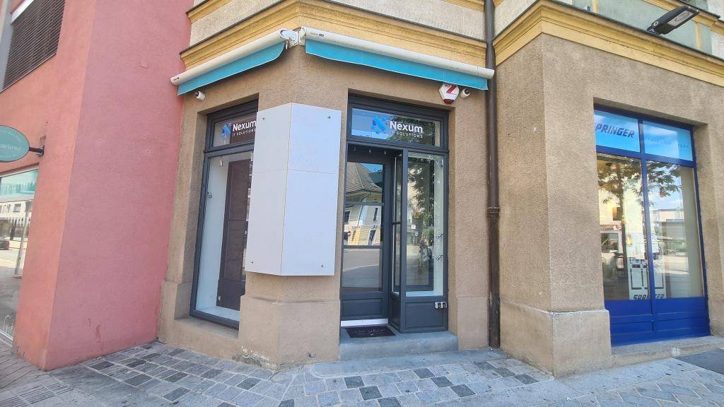 Geschäftseingang mit großen Glasfenstern und einer blauen Markise an einer belebten Straßenecke.