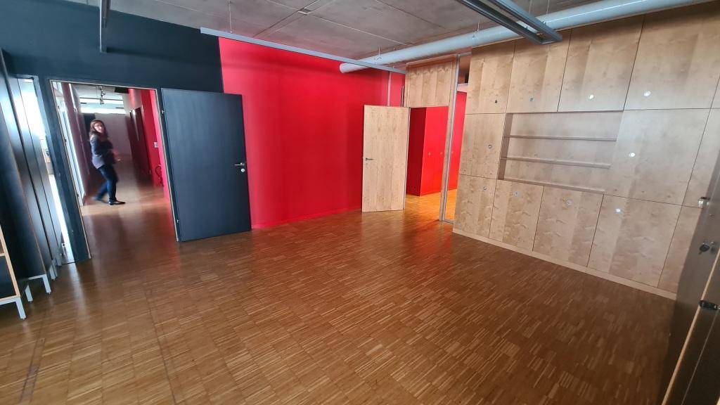 Büroraum mit auffälligen roten Wänden, Holzparkettboden und integrierten Holzschränken, die einen modernen Kontrast bilden.