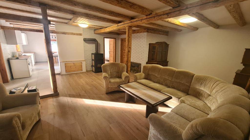 Geräumiges Wohnzimmer mit bequemen Sofas, rustikalen Holzbalken und einem Kaminofen.