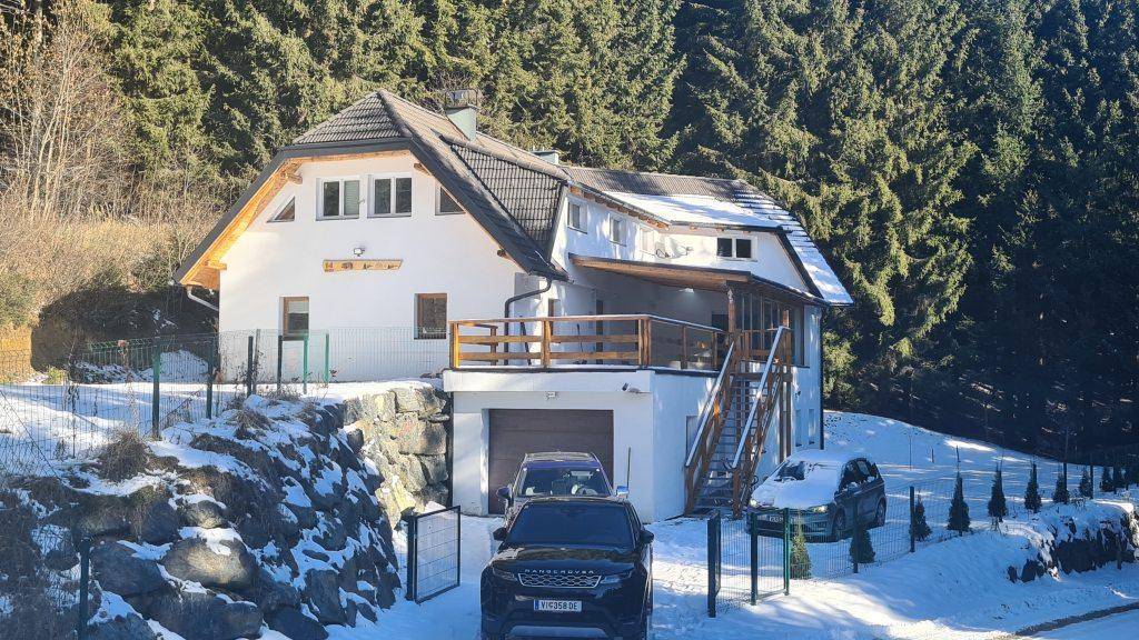 Modernes Haus im Schnee mit Wald im Hintergrund und einer Einfahrt.