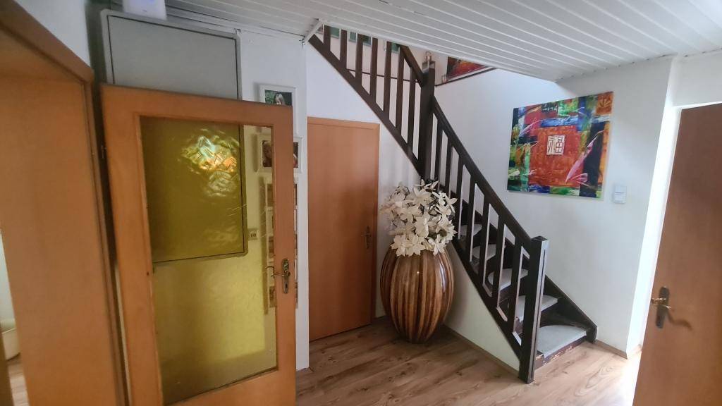 Heller Eingangsbereich mit dunkler Holztreppe und dekorativer Vase.