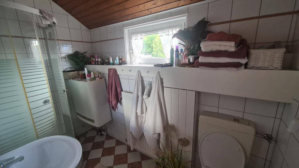 Badezimmer im Dachgeschoss mit Dusche, WC und Fenster mit Blick ins Grüne.
