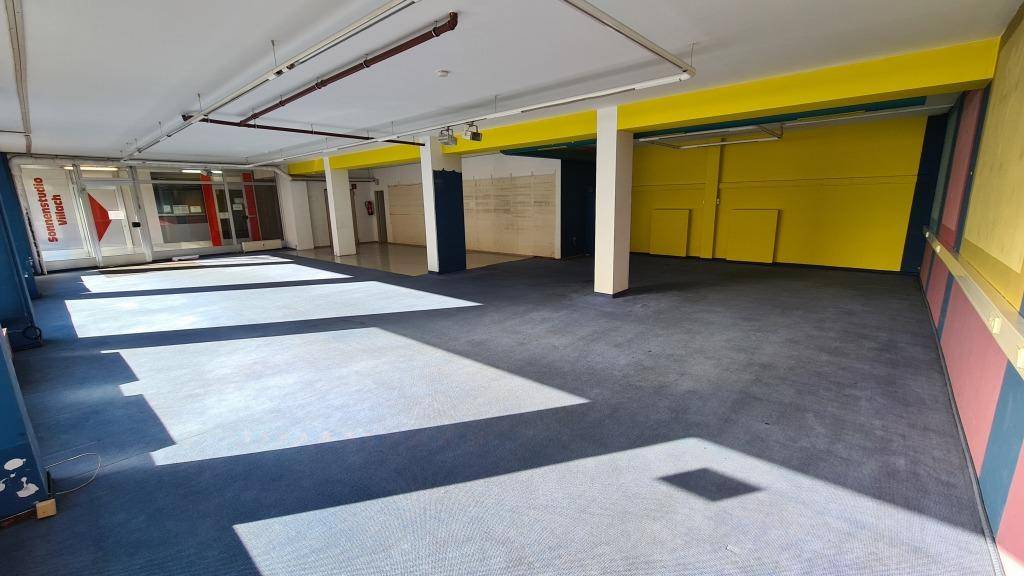 Geräumiger Gewerberaum mit blauem Teppichboden und gelb gestrichenen Wänden, durchflutet von Tageslicht.