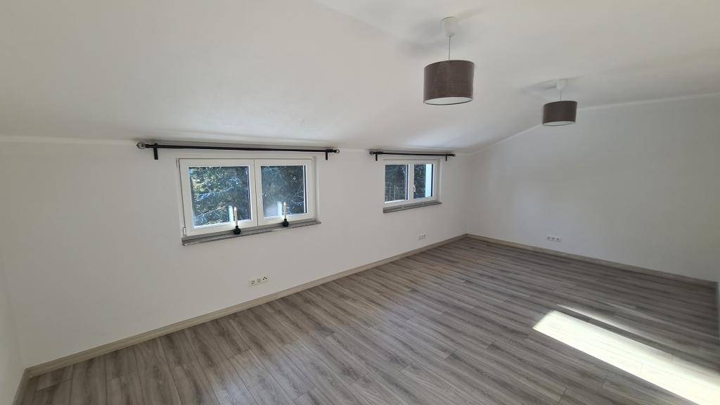 Helles Dachgeschosszimmer mit Schrägen, Holzboden und zwei Fenstern.