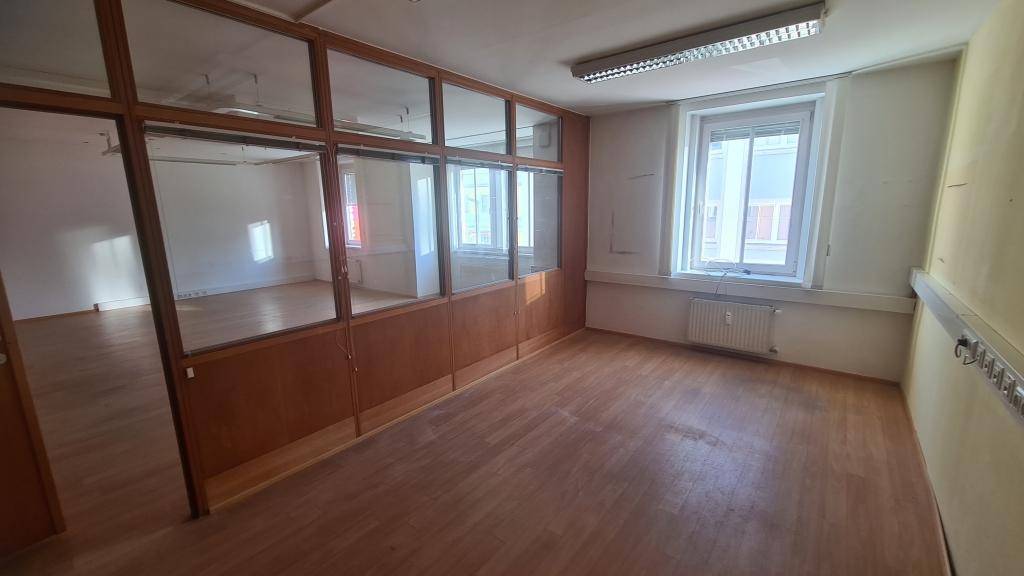 Büro mit Holzboden, großen Fenstern und Glaswand, die den Raum in zwei Bereiche teilt.