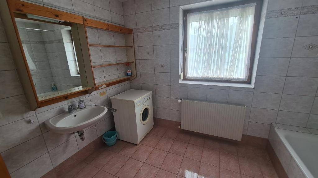 Helles Badezimmer mit Waschbecken, Waschmaschine und Fenster, komplett gefliest.