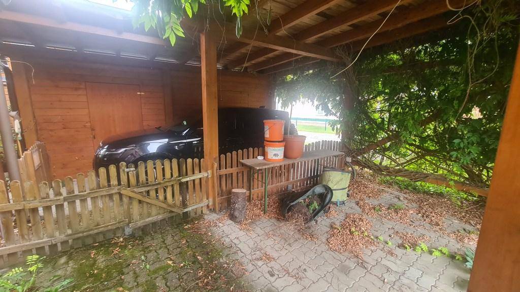Überdachter Stellplatz für ein Fahrzeug mit Holzzaun und üppiger Begrünung im Außenbereich.