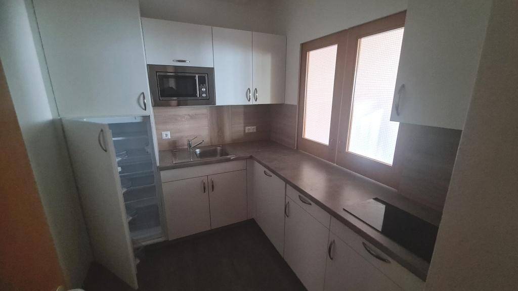 Moderne Küchenzeile mit weißen Schränken, integrierter Mikrowelle und Kühlschrank, ideal für kleine Pausen.