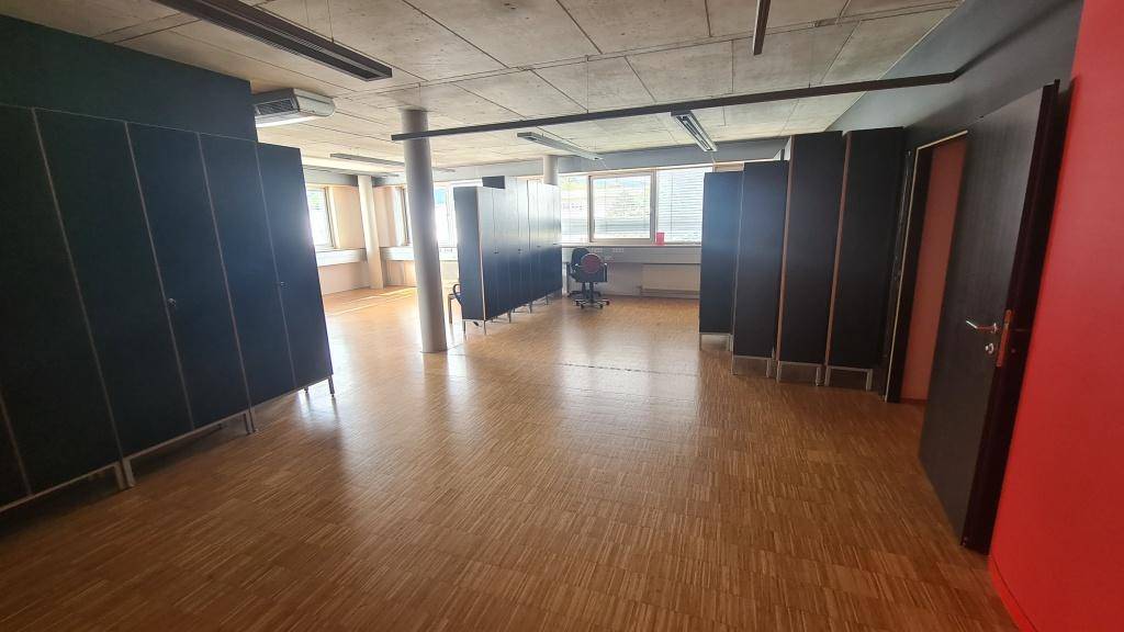 Geräumiger Büroraum mit Holzparkettboden, langen Fensterfronten und schwarzen Schränken, die viel Stauraum bieten.