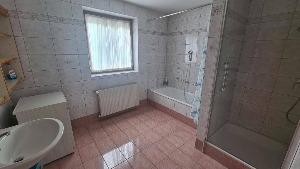 Gefliestes Badezimmer mit Badewanne, Dusche und Fenster, bietet ausreichend Tageslicht.