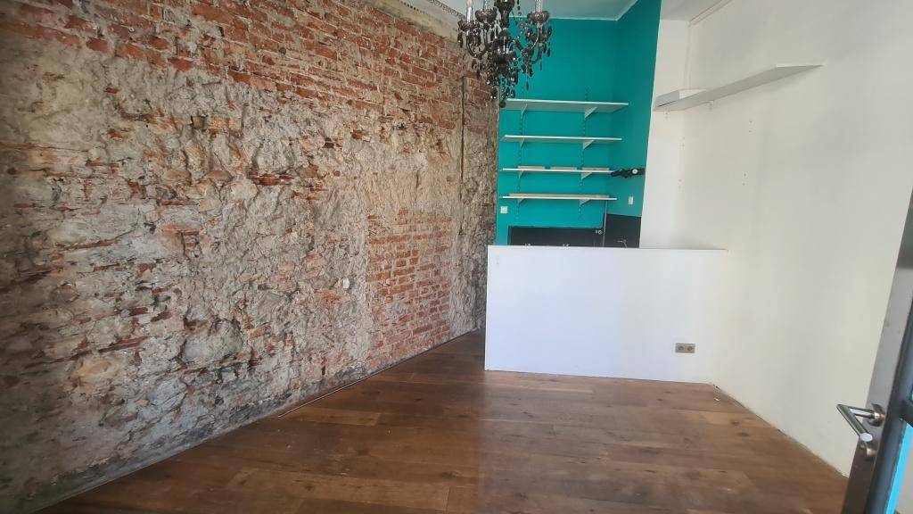 Innenraum mit freigelegter Ziegelwand, Holzboden und einer türkisen Wand mit Regalsystem.
