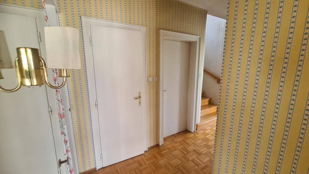 Heller Flur mit gelb-gestreifter Tapete, weißen Türen und Holzparkettboden.