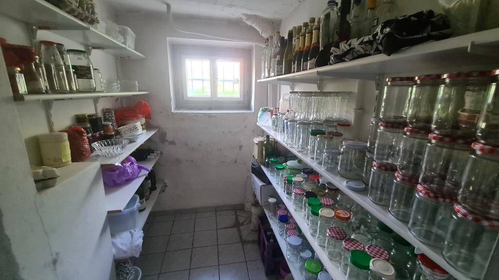 Vorratsraum im Keller mit Regalen voller Gläser und einem kleinen Fenster.