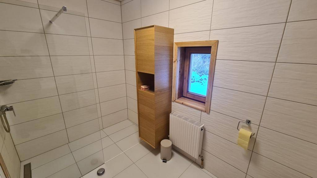 Badezimmer mit begehbarer Dusche, weißen Fliesen und einem Fenster für Tageslicht.