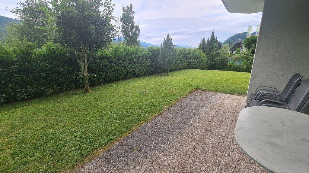 Gedeckte Terrasse mit Fliesenboden und Gartenmöbeln, umgeben von einer hohen Hecke.