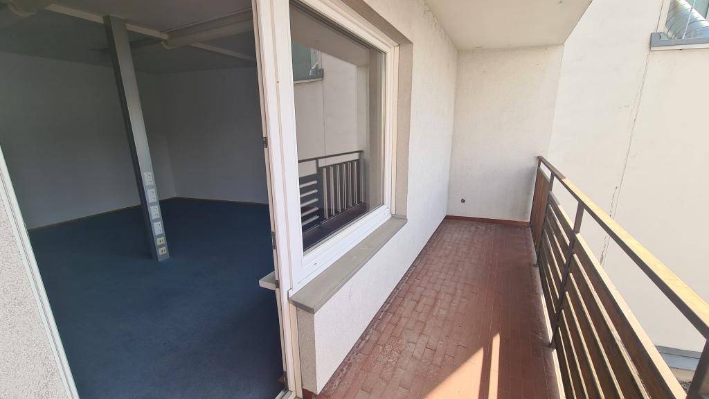 Schmaler Balkon mit Metallgeländer, der einen Blick in einen leeren Raum mit blauem Teppichboden ermöglicht.