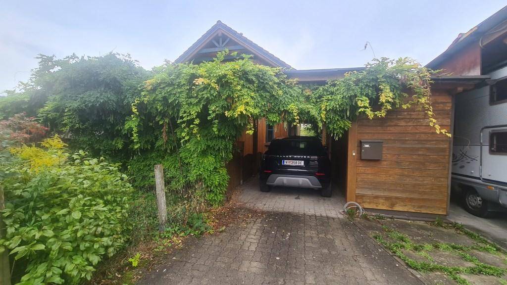 Außenansicht des Hauses mit überdachtem Stellplatz und üppiger grüner Bepflanzung.