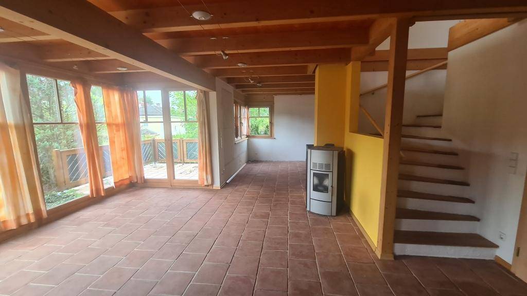 Heller Wohnbereich mit Terrakotta-Fliesenboden, Holzdecke und einem modernen Kaminofen.