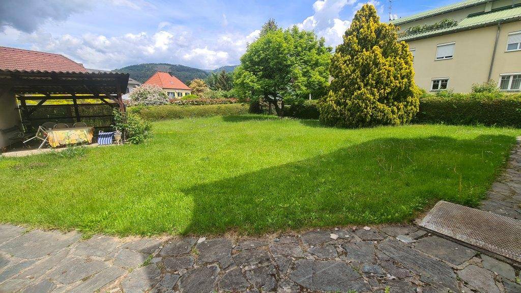 Großer, gepflegter Rasenbereich im Garten mit Bäumen und einer überdachten Terrasse.