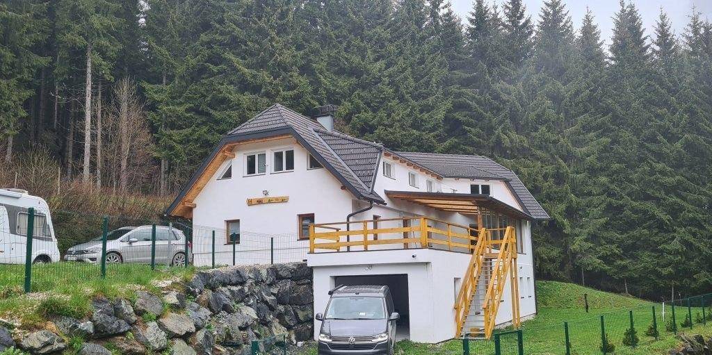 Modernes Wohnhaus in ländlicher Umgebung mit Wald im Hintergrund und integrierter Garage.