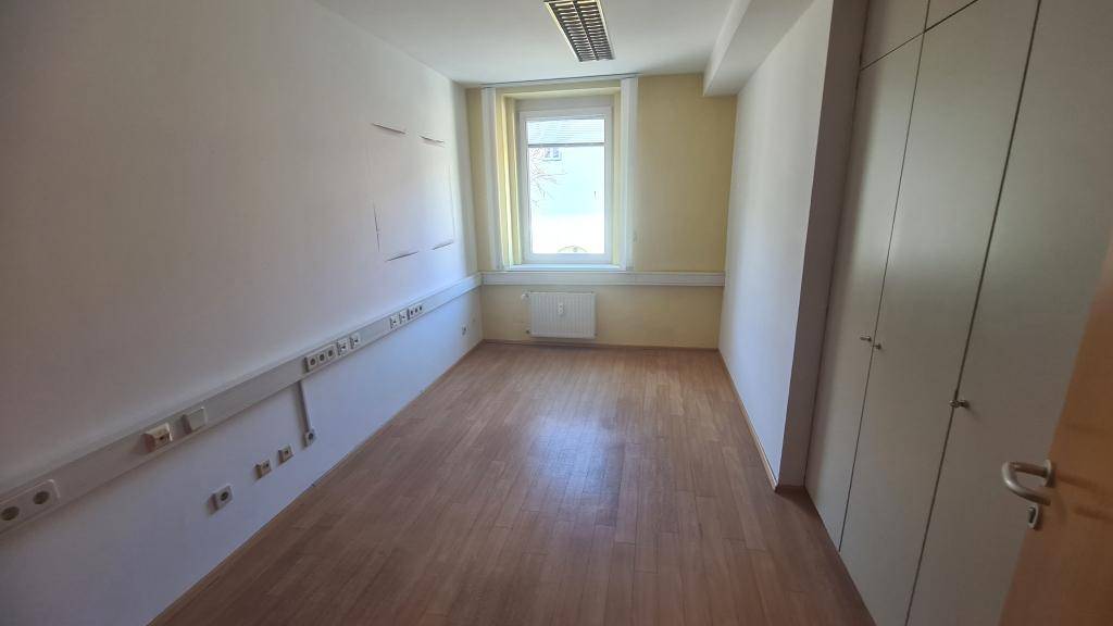 Büro mit Holzboden, Fenster und Einbauschränken, ausgestattet mit vielen Steckdosenleisten.