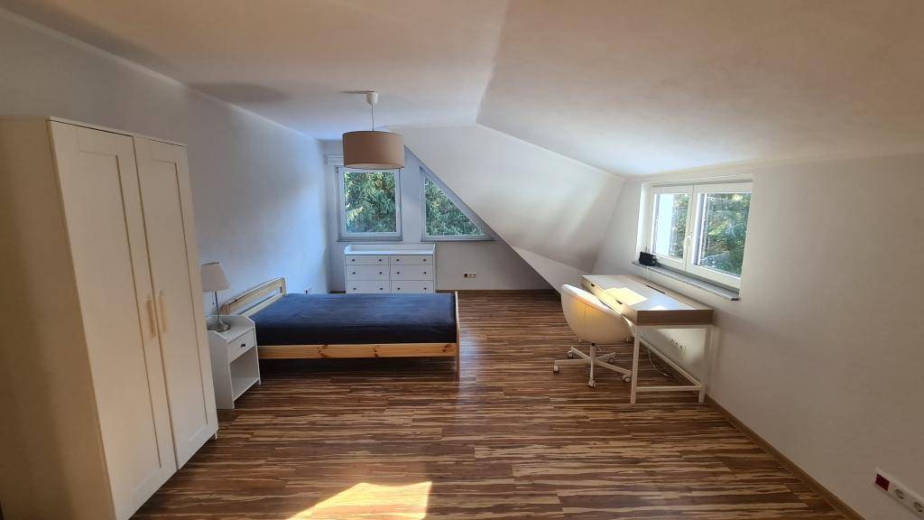 Helles Schlafzimmer im Dachgeschoss mit Schrägen, Holzboden und mehreren Fenstern.