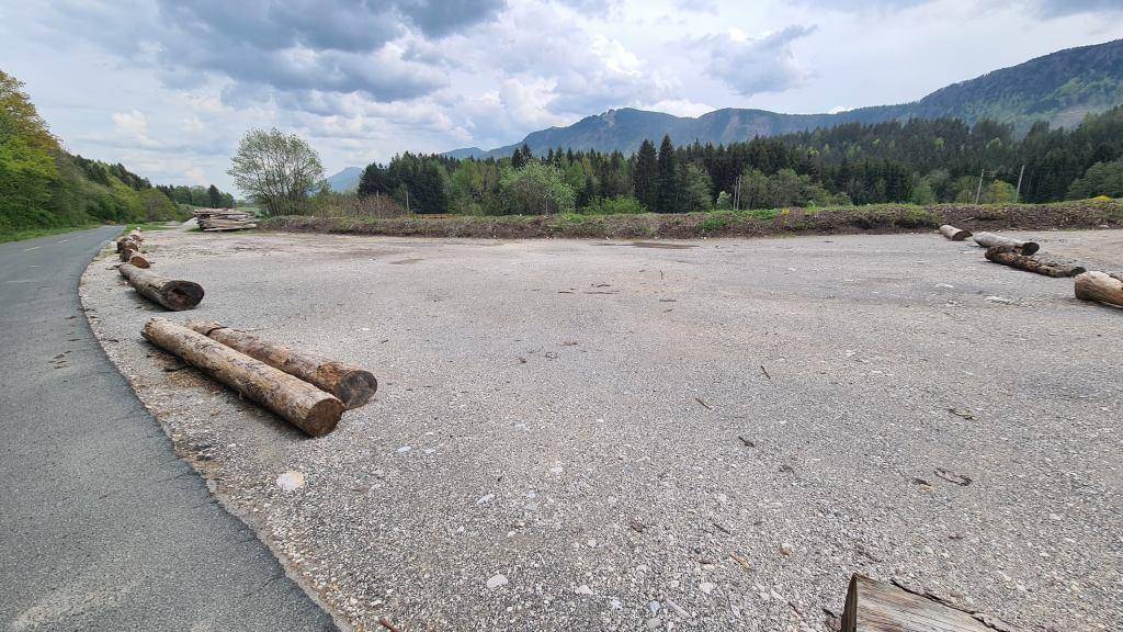 Große Schotterfläche mit Baumstämmen am Rand und weitem Blick auf die umliegenden Berge.