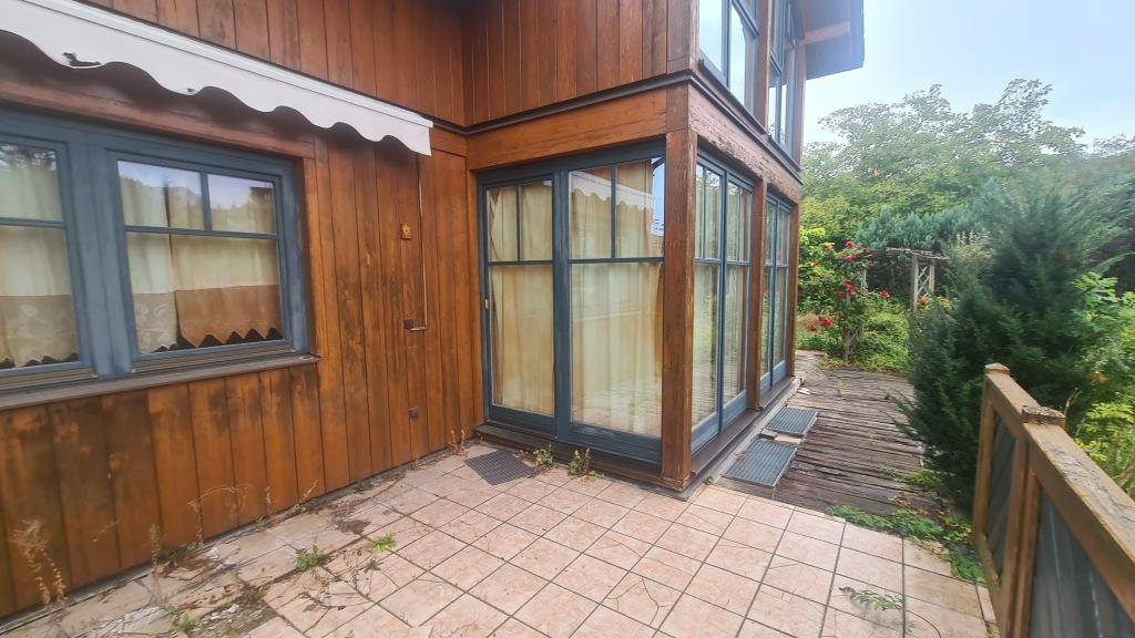 Gepflasterte Terrasse am Haus mit Zugang zu großen Fenstern und umrankt von Rosen.