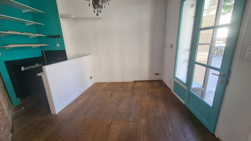Leerer Geschäftsraum mit Holzboden, weißen Wänden und einer auffälligen türkisen Akzentwand mit Regalen.