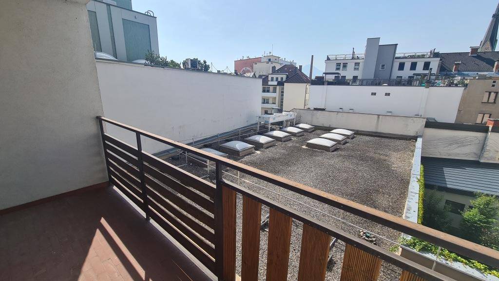 Balkon mit Holz- und Metallgeländer, bietet einen weiten Blick über die Dächer und die Stadtlandschaft.