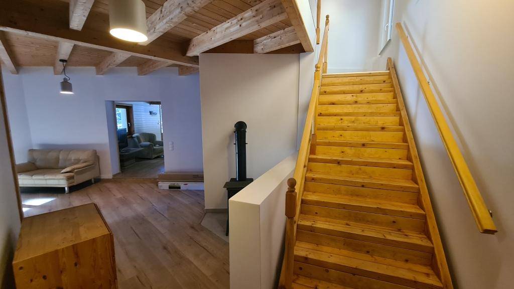 Helle Holztreppe führt in den oberen Bereich, mit Kaminofen im Flur.